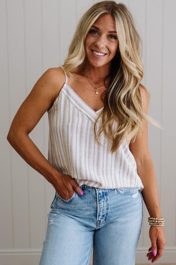 Woman wearing a white ribbed tank top and blue jeans with a neutral background