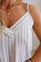 Close-up of a person wearing a gold necklace with a lock pendant and a white sleeveless top.