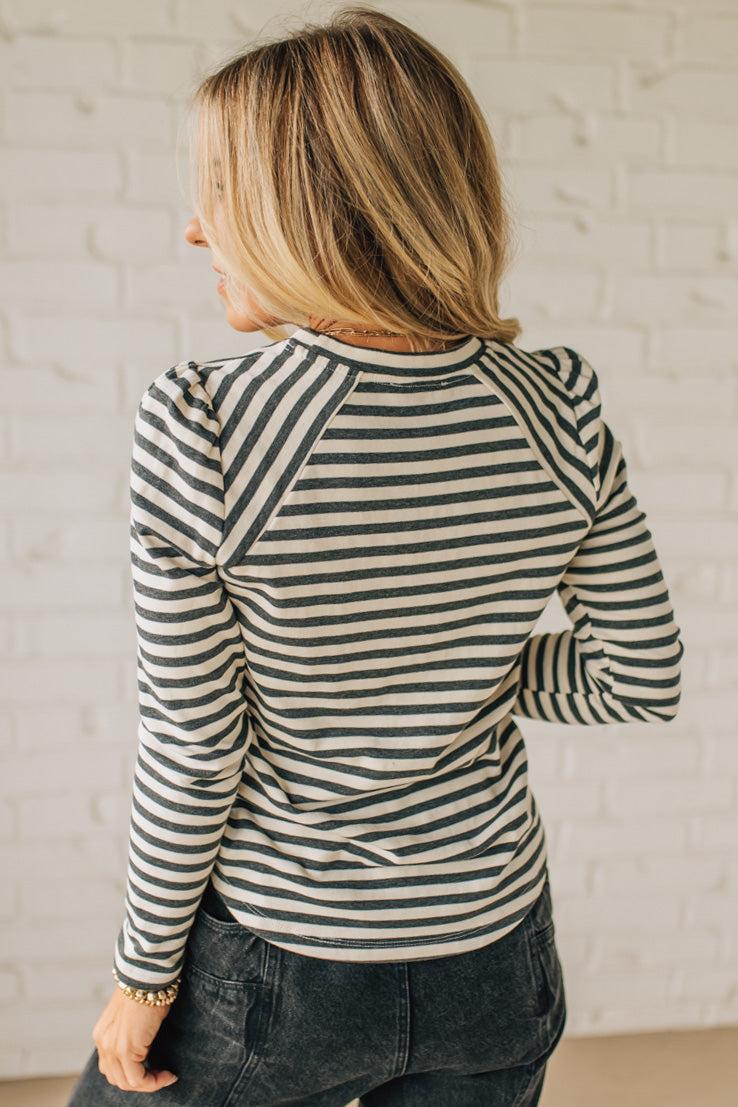 Woman wearing a striped long-sleeve top against a white brick wall.