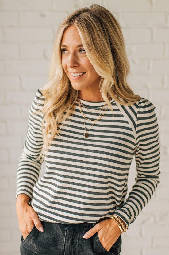 Woman wearing a striped long-sleeve shirt against a white brick wall