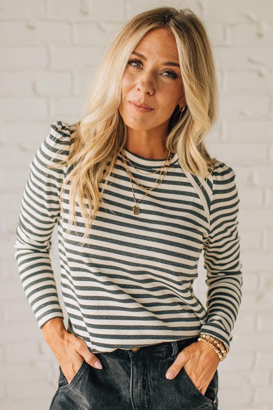 Woman wearing a striped long-sleeve shirt against a white brick wall.