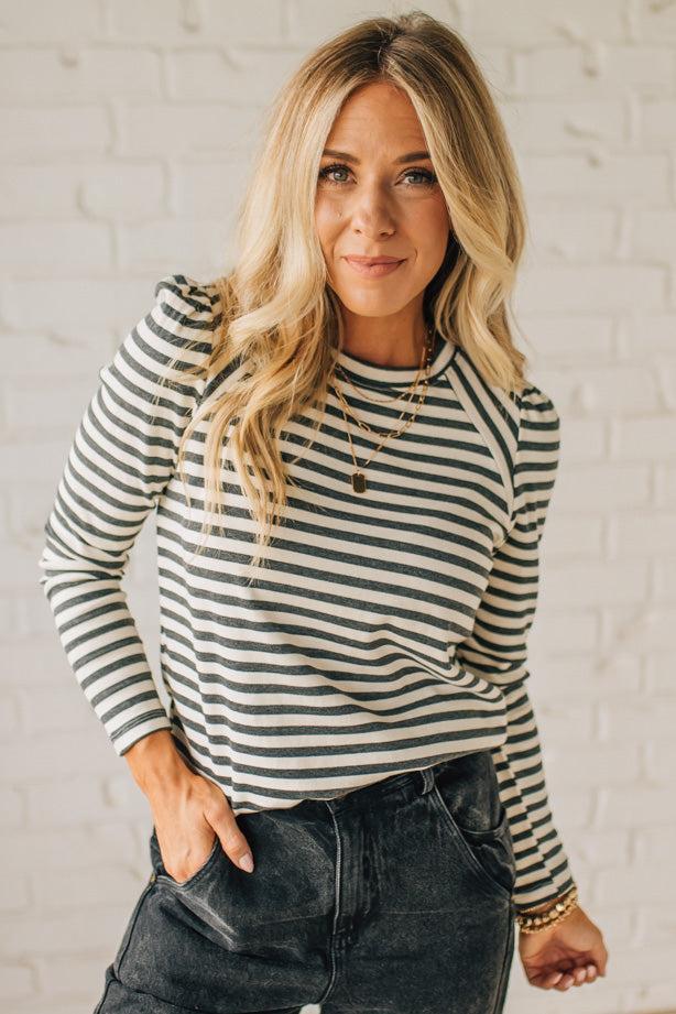 Woman wearing a striped shirt against a white brick wall