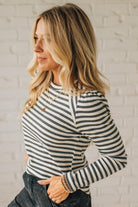 Woman wearing a striped long-sleeve top against a white brick wall.