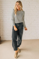 Woman wearing a striped sweater and dark jeans standing against a white brick wall.