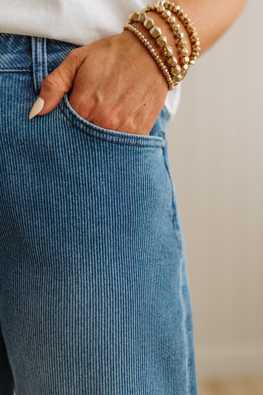 Person wearing blue jeans with gold bracelets on a neutral background