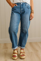 Person wearing blue jeans and sandals standing against a neutral wall.