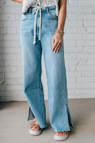 BLONDE WOMAN WEARING DRAWSTRING WAIST DETAIL STRETCH SIDE SLIT WIDE LEG JEAN IN MEDIUM BLUE.