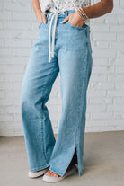 BLONDE WOMAN WEARING DRAWSTRING WAIST DETAIL STRETCH SIDE SLIT WIDE LEG JEAN IN MEDIUM BLUE.