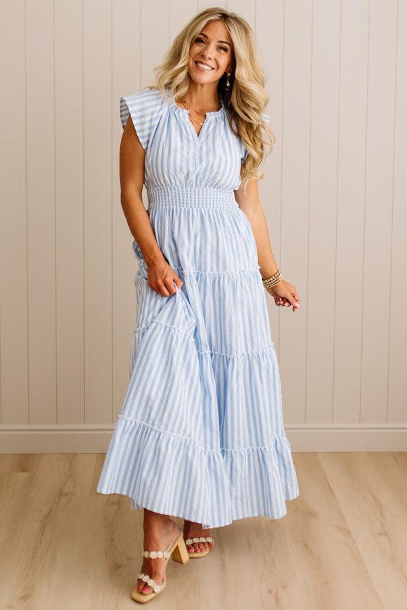 Woman wearing a blue and white striped dress against a beige wall.