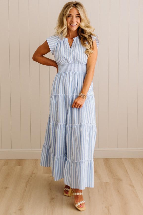 Woman wearing a light blue and white striped dress against a beige wall.