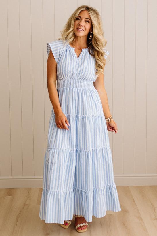 Woman wearing a light blue striped dress against a beige wall.