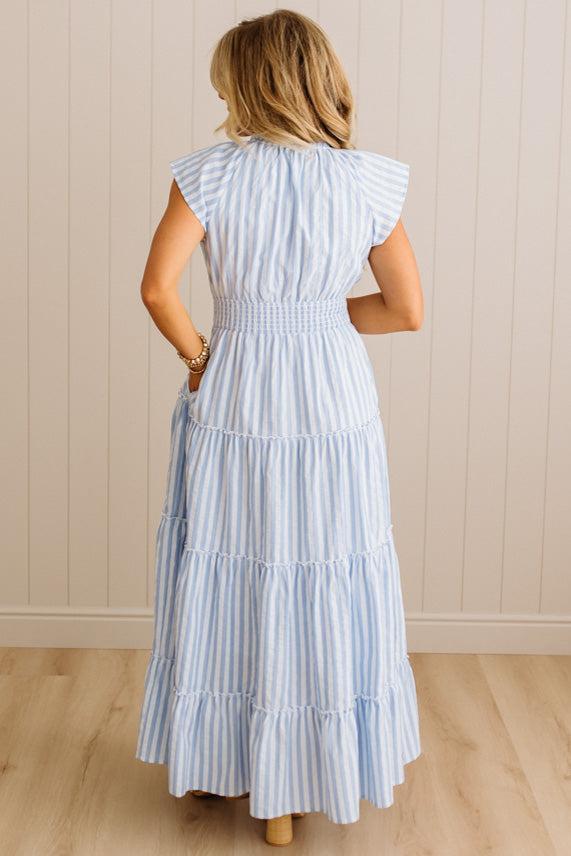 Woman wearing a light blue and white striped dress against a beige wall.