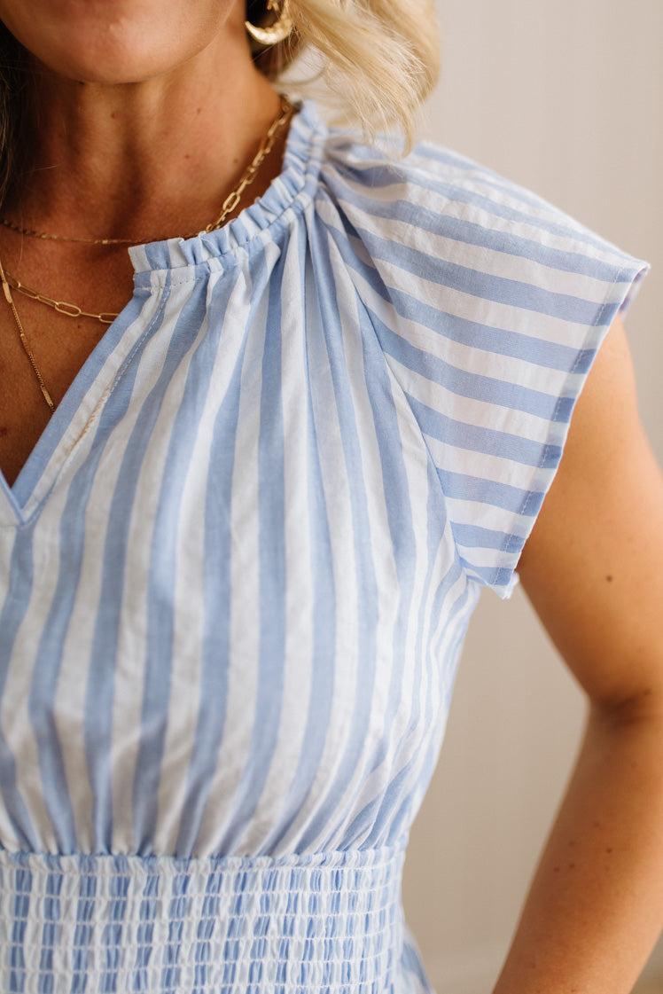 Close-up of a person wearing a blue and white striped dress with a neutral background