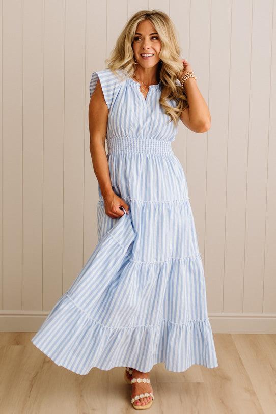 Woman wearing a light blue striped dress against a beige wall.