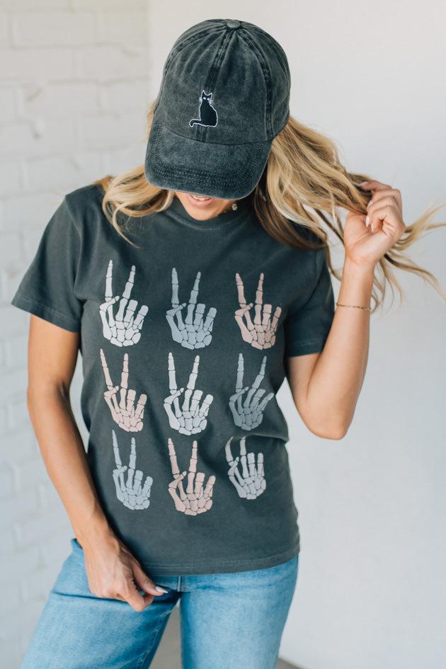 Person wearing a dark green t-shirt with hand gesture designs and a matching cap.