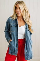 Woman wearing a denim jacket, white top, and red pants against a light background