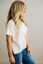 Woman wearing a sand beige t-shirt and blue jeans against a neutral background