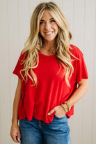 Woman wearing a red shirt and blue jeans against a light wooden panel background