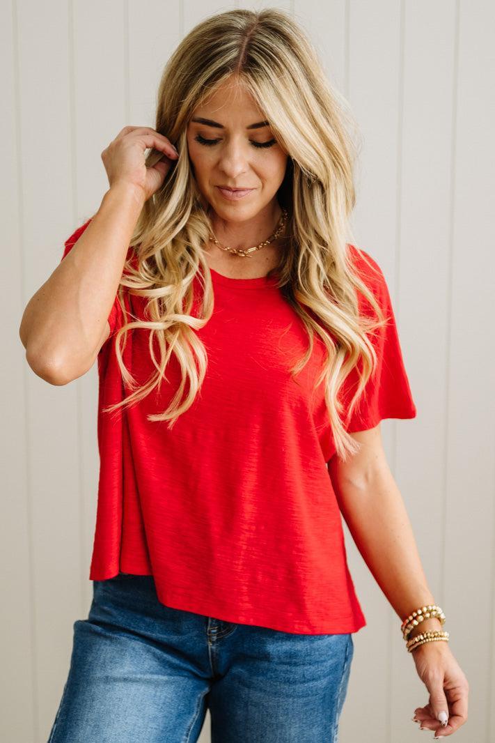Woman wearing a red top and blue jeans against a plain background