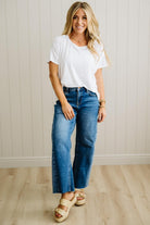 Woman wearing a white t-shirt and blue jeans standing against a light wooden paneled wall.
