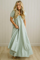 Woman wearing a green checkered dress standing against a beige wall.