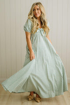 Woman wearing a green checkered dress standing against a wooden paneled wall.
