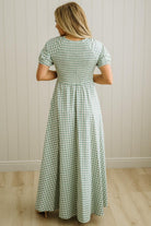 Woman wearing a green and white checkered dress against a white paneled wall.