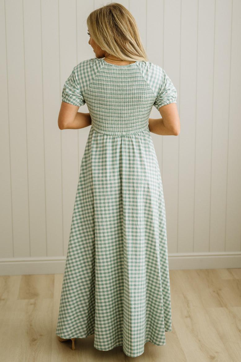 Woman wearing a green and white checkered dress against a white paneled wall.