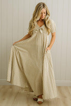 Woman wearing a checkered dress standing in a room with wooden flooring and a white paneled wall.