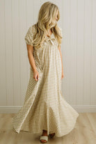 Woman wearing a checkered dress standing against a white paneled wall.