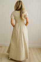 Woman wearing a checkered dress standing against a white paneled wall.
