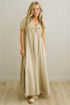 Woman wearing a checkered dress standing against a light wooden paneled wall.