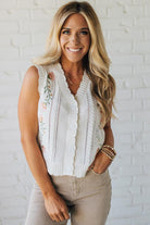 Blonde woman wearing a cream vest with scallop trim and floral embroidery.