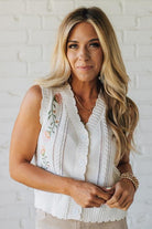 Blonde woman wearing a cream vest with scallop trim and floral embroidery.