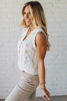 Blonde woman wearing a cream vest with scallop trim and floral embroidery.