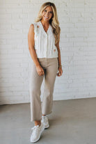 Blonde woman wearing a cream vest with scallop trim and floral embroidery.