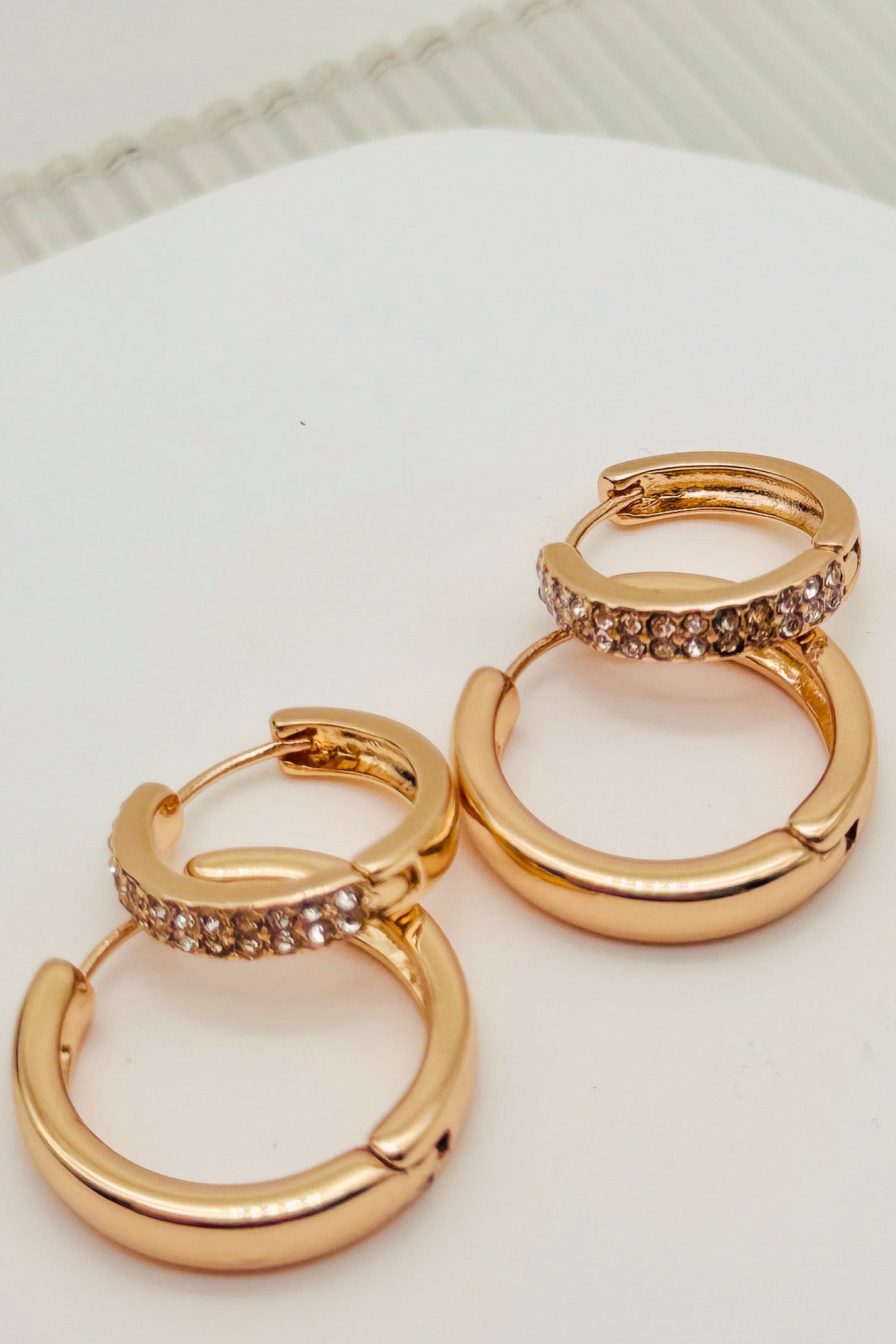 Pair of rose gold hoop earrings with embedded stones on a white surface.