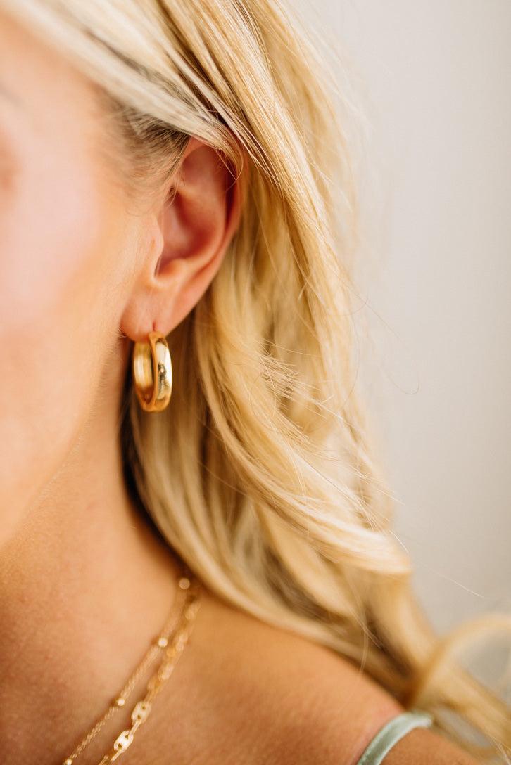 Close-up of a person wearing gold hoop earrings and a delicate necklace.