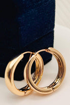 Pair of gold hoop earrings on a white surface with a dark blue velvet box in the background.