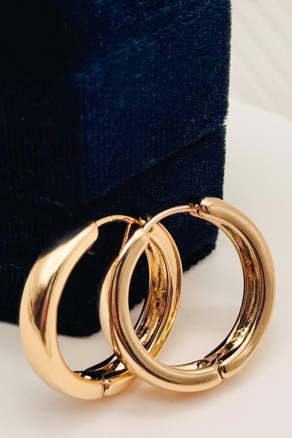 Pair of gold hoop earrings on a white surface with a dark blue velvet box in the background.