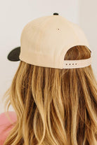 Blonde woman wearing a cream and black trucker hat with "SOMEBODY'S PROBLEM" embroidered at the front in pink and black.