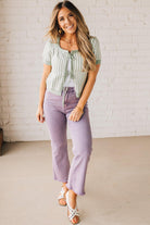 BLONDE WOMAN IN PURPLE PANTS WEARING A LIGHT GREEN AND WHITE TIE FRONT TEXTURED VERTICAL STRIPE SCOOP NECK KNIT SWEATER WITH DOUBLE TIES.