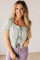 BLONDE WOMAN IN PURPLE PANTS WEARING A LIGHT GREEN AND WHITE TIE FRONT TEXTURED VERTICAL STRIPE SCOOP NECK KNIT SWEATER WITH DOUBLE TIES.