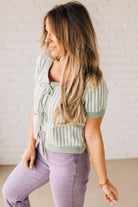 BLONDE WOMAN IN PURPLE PANTS WEARING A LIGHT GREEN AND WHITE TIE FRONT TEXTURED VERTICAL STRIPE SCOOP NECK KNIT SWEATER WITH DOUBLE TIES.