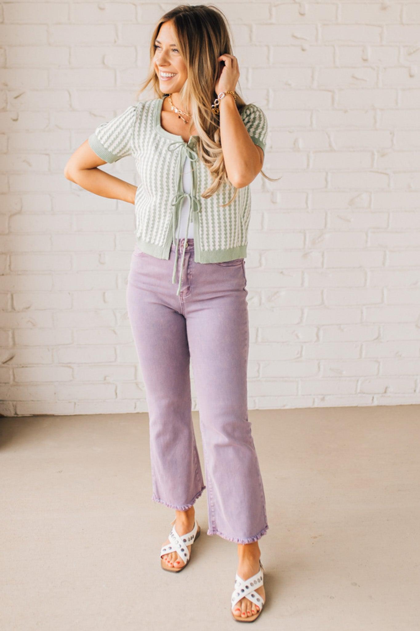 BLONDE WOMAN IN PURPLE PANTS WEARING A LIGHT GREEN AND WHITE TIE FRONT TEXTURED VERTICAL STRIPE SCOOP NECK KNIT SWEATER WITH DOUBLE TIES.