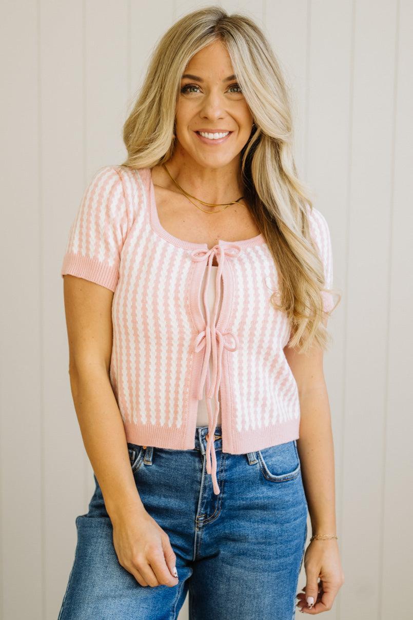 Woman wearing a pink striped top with a tie and blue jeans against a neutral background