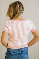 Person wearing a pink and white patterned short-sleeve sweater and blue jeans against a neutral background
