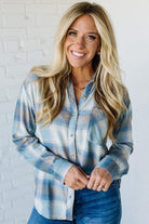 Woman wearing a blue plaid shirt against a white brick wall