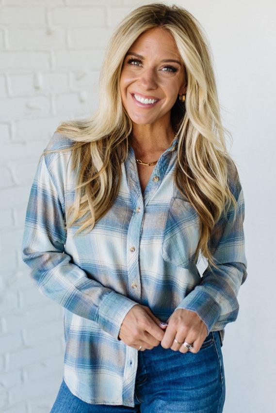 Woman wearing a blue plaid shirt against a white brick wall