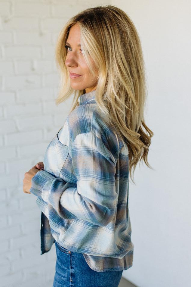 Woman wearing a blue plaid shirt against a white brick wall